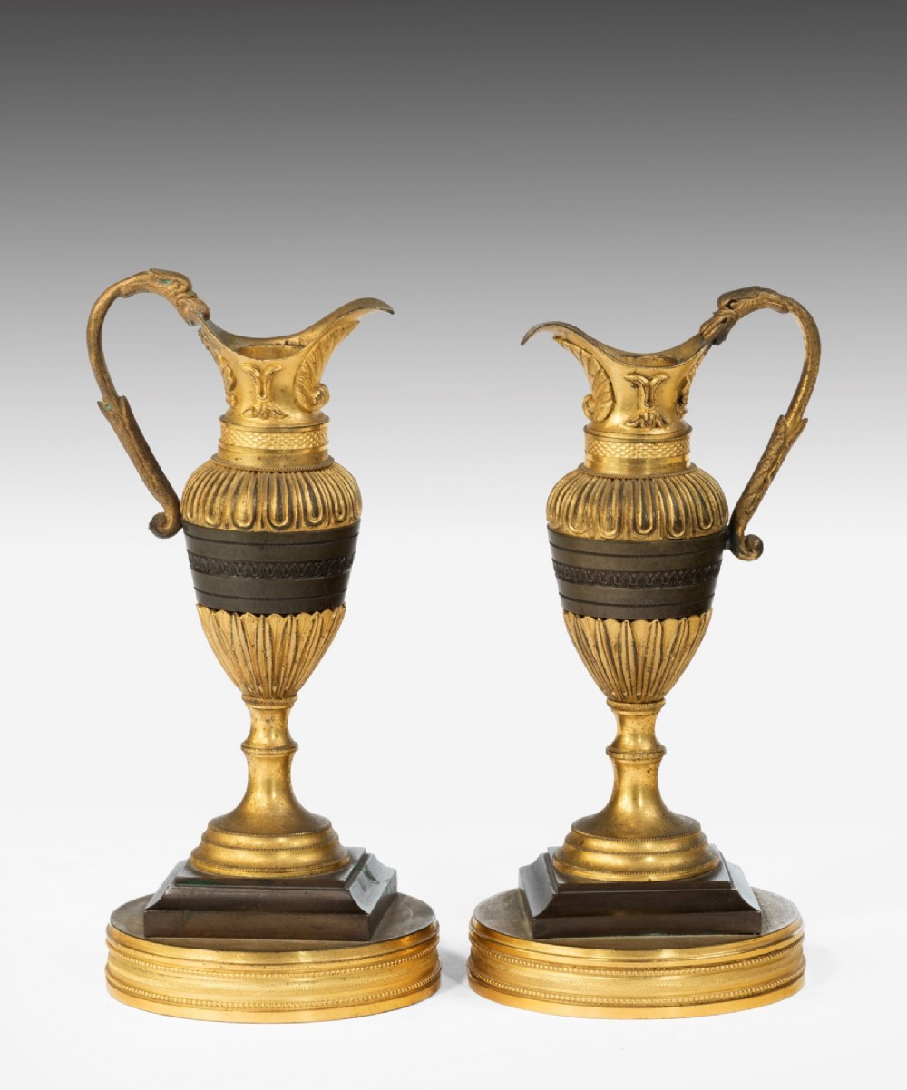 A pair of 19th-century Neoclassical ewers featuring reeded gilt-bronze urn bodies with dark patinated bronze central bands, cast handles, and tiered bases. View II