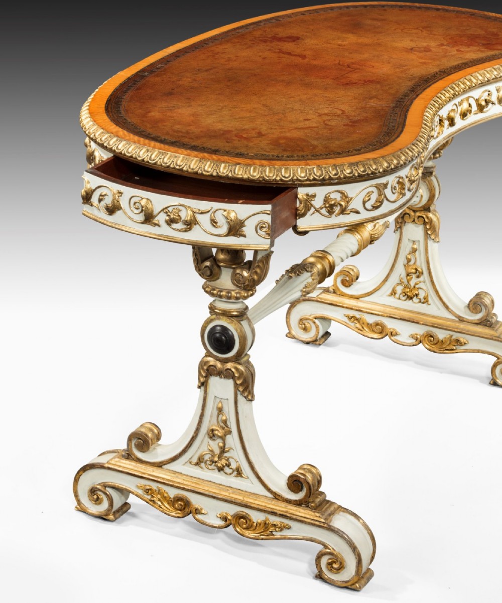 A kidney-shaped William IV writing table featuring an ivory-painted finish, detailed carved giltwood embellishments, a turned stretcher, and a brown leather inset surface. View III