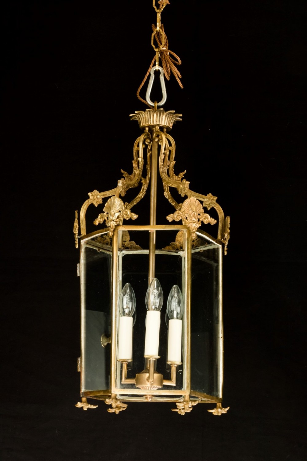 An antique Neo-Classical brass hanging hall lantern featuring glazed glass panels and three internal candle-style lights.