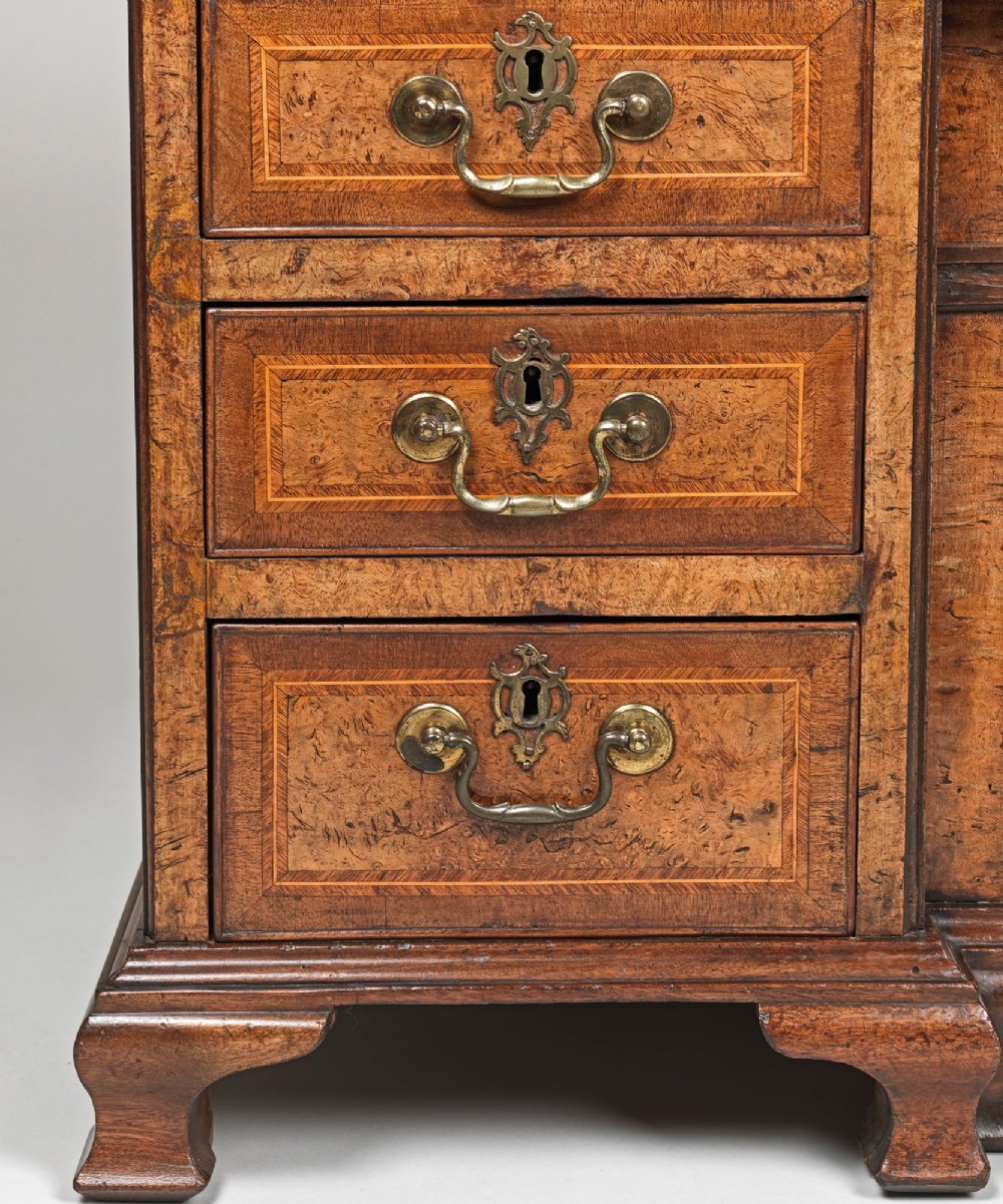 A George II burr elm kneehole desk featuring a long top drawer over six side drawers surrounding a central recessed cupboard on shaped bracket feet. View II