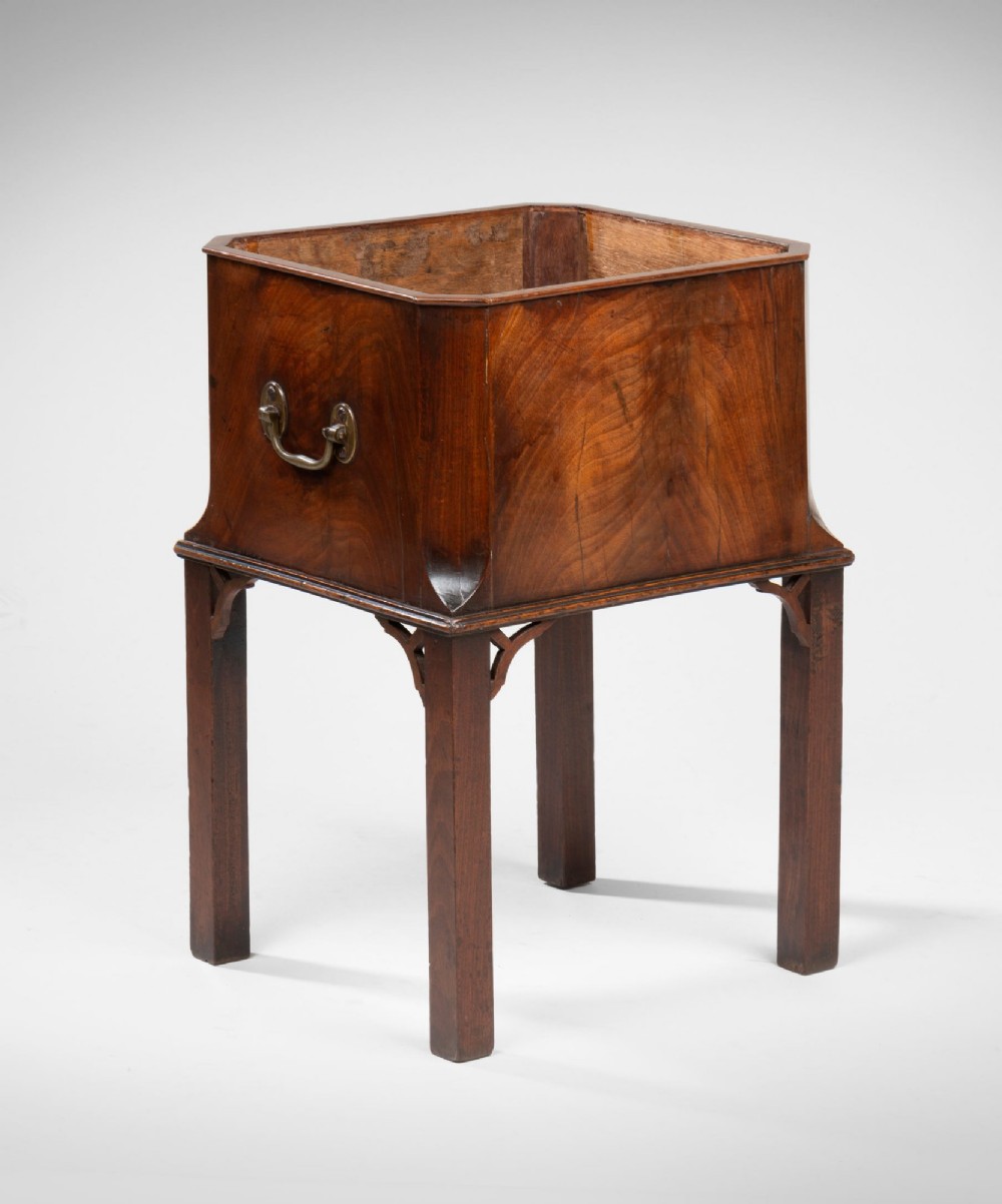 A Georgian Chippendale mahogany wine cooler on a four-legged stand featuring canted corners, brass carrying handles, and fretwork corner spandrels.