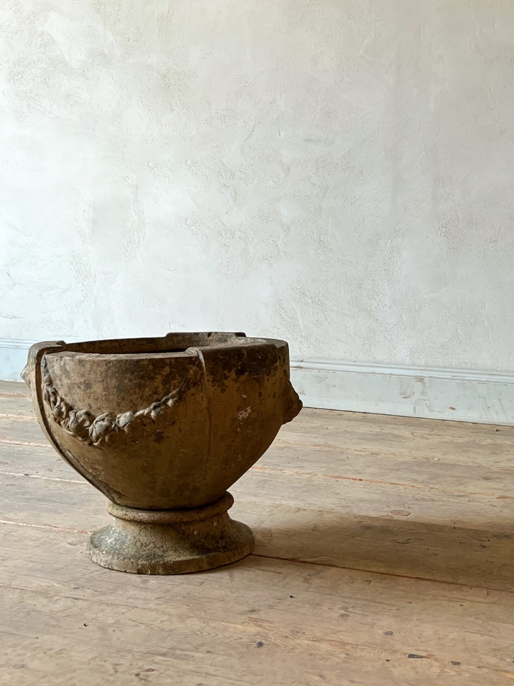 A round buff terracotta garden planter featuring carved relief floral garlands and a pedestal base.