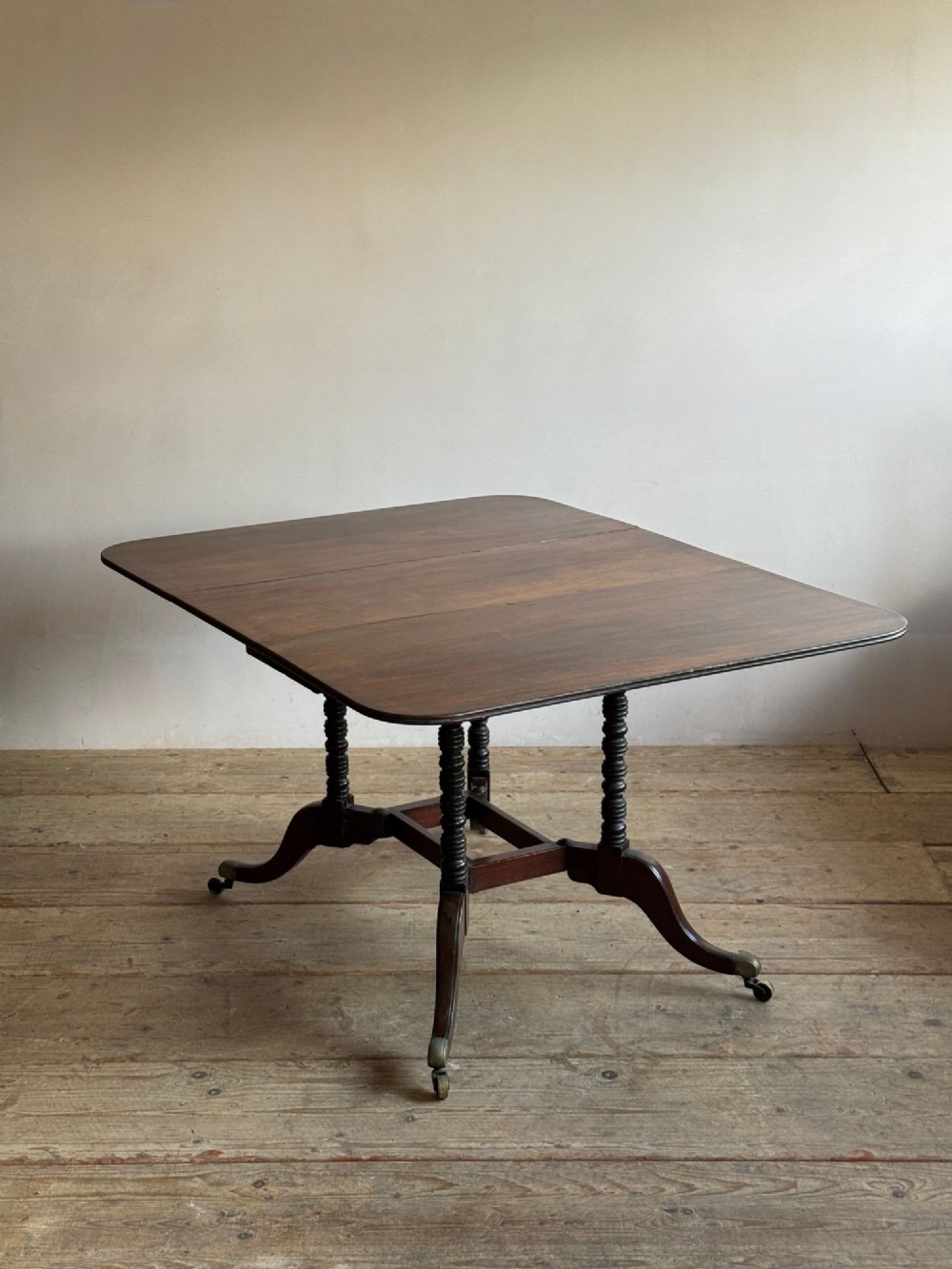 A dark mahogany Georgian Cumberland drop-leaf dining table with bobbin-turned dual legs, splayed feet, and brass castors. View II