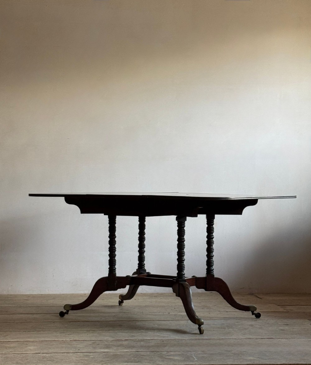 A dark mahogany Georgian Cumberland drop-leaf dining table with bobbin-turned dual legs, splayed feet, and brass castors. View III