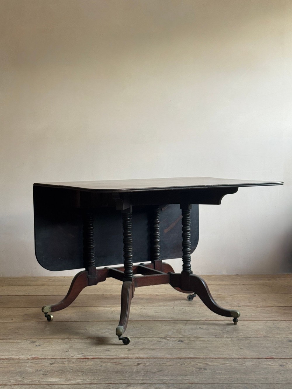 A dark mahogany Georgian Cumberland drop-leaf dining table with bobbin-turned dual legs, splayed feet, and brass castors. View IV