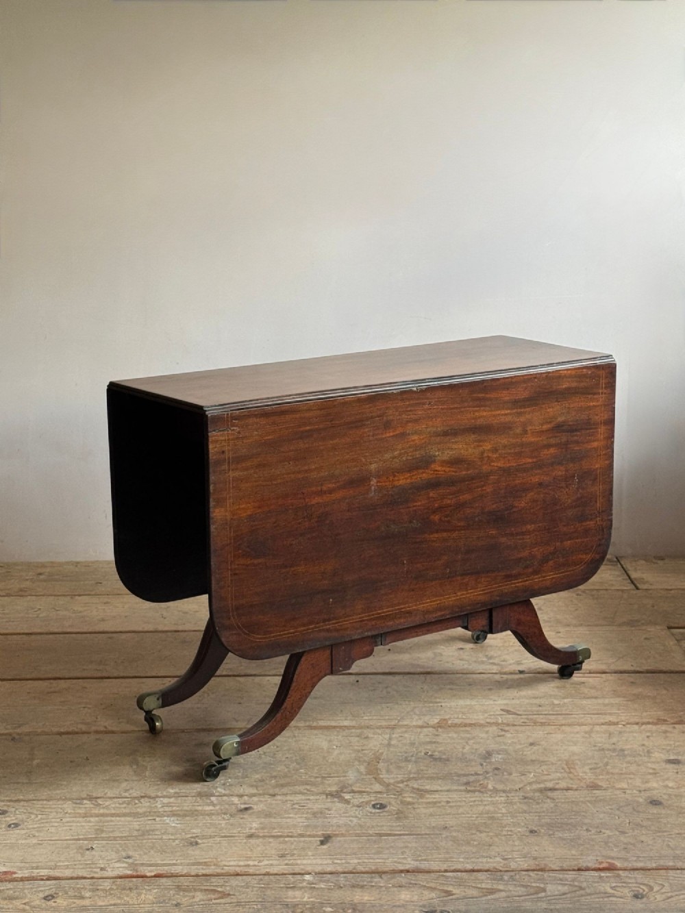 A dark mahogany Georgian Cumberland drop-leaf dining table with bobbin-turned dual legs, splayed feet, and brass castors. View V