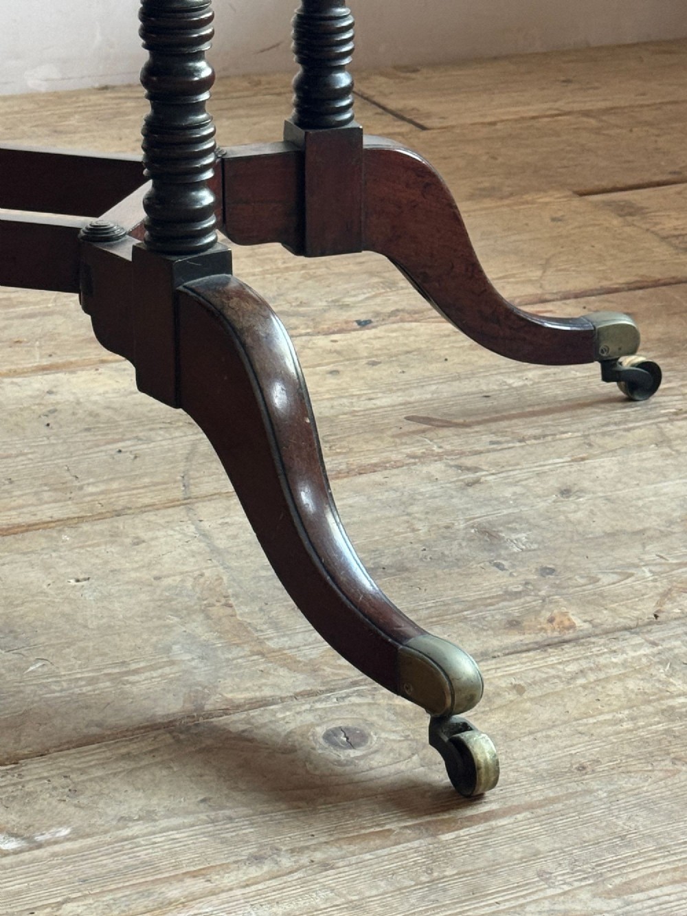 A dark mahogany Georgian Cumberland drop-leaf dining table with bobbin-turned dual legs, splayed feet, and brass castors. View VI