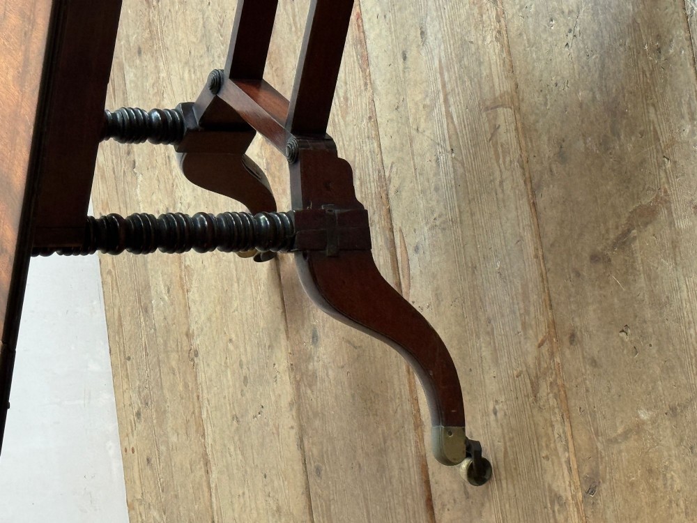 A dark mahogany Georgian Cumberland drop-leaf dining table with bobbin-turned dual legs, splayed feet, and brass castors. View VII