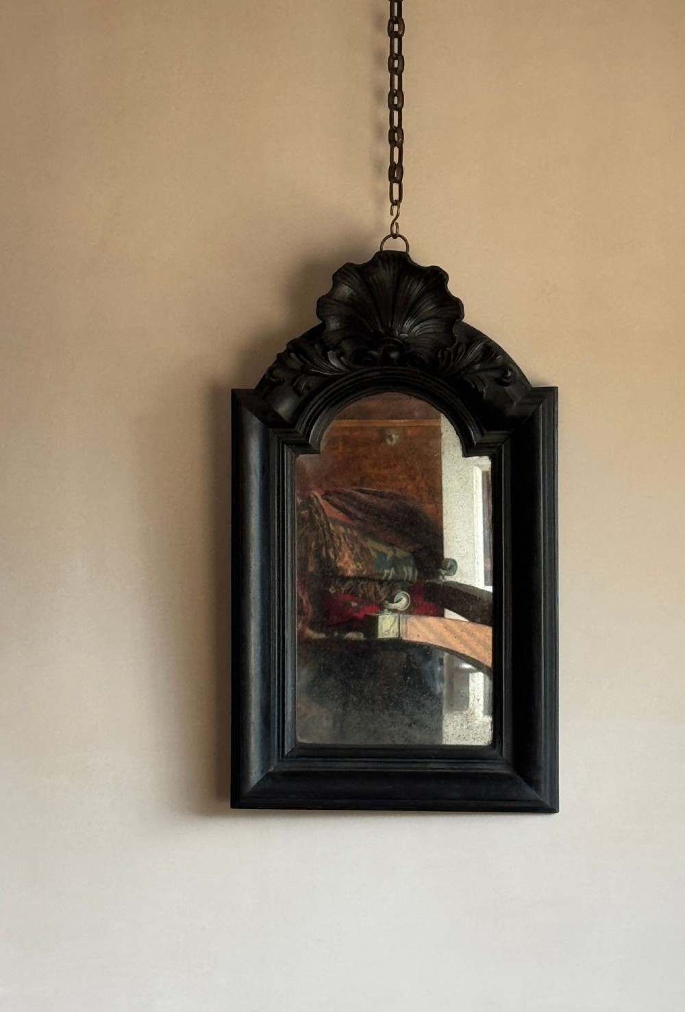 A nineteenth-century ebonised wall mirror with a carved shell cresting and arched frame, suspended from a metal chain.