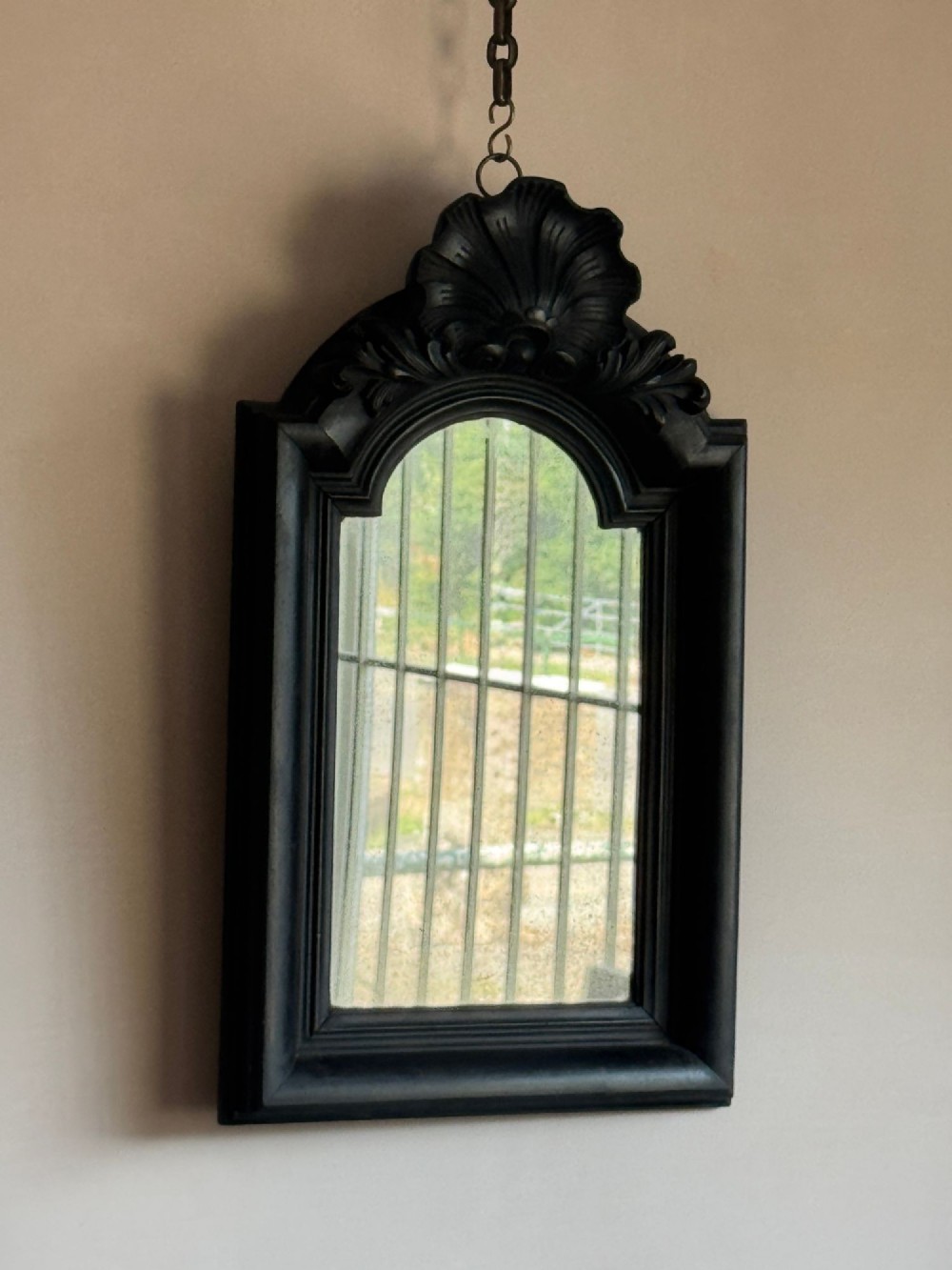 A nineteenth-century ebonised wall mirror with a carved shell cresting and arched frame, suspended from a metal chain. View II