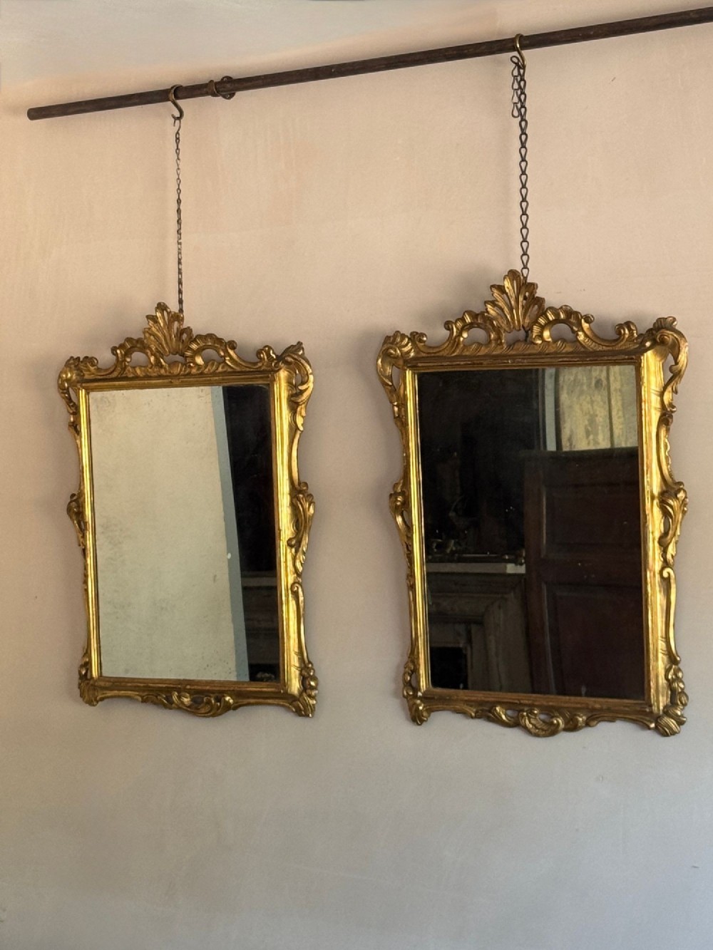 A symmetrical pair of rectangular wall mirrors framed in carved gold giltwood with acanthus leaf cresting and rococo scroll details.