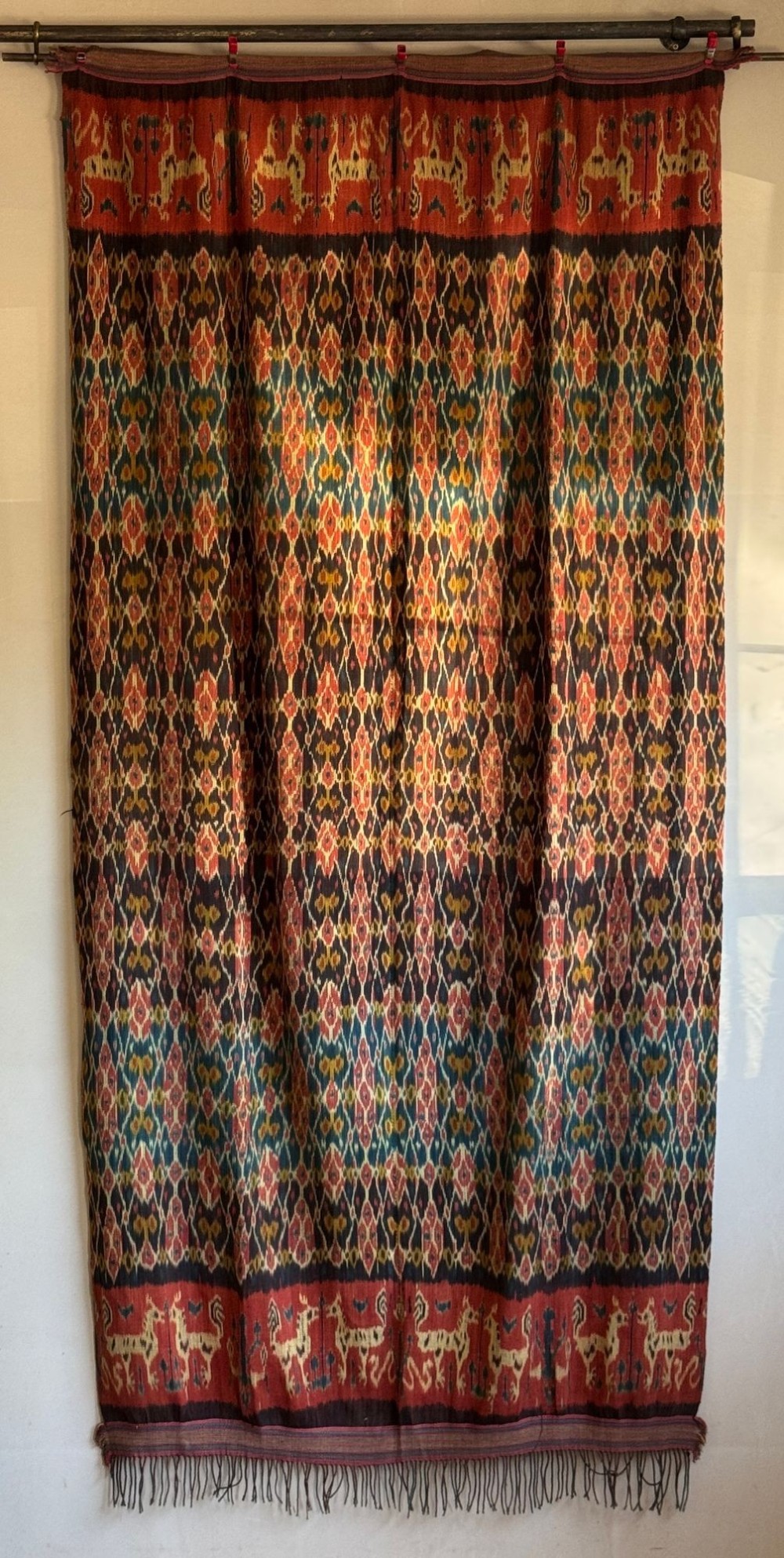 A vertical handwoven Sumba ikat hinggi textile featuring diamond lattice patterns in terracotta red, dark indigo, and yellow with zoomorphic border bands and lower fringe. View II