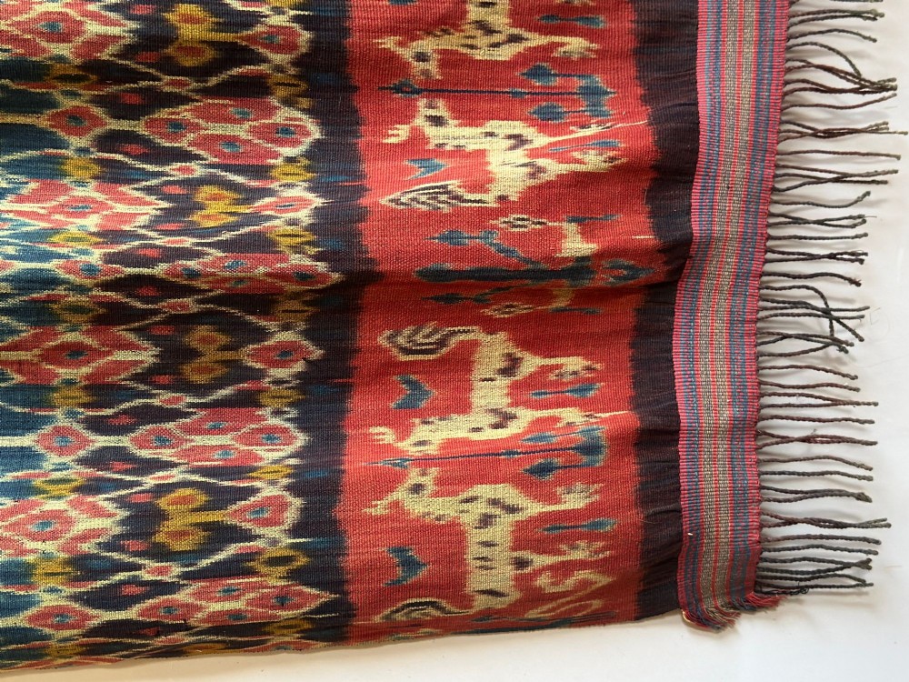 A vertical handwoven Sumba ikat hinggi textile featuring diamond lattice patterns in terracotta red, dark indigo, and yellow with zoomorphic border bands and lower fringe. View III