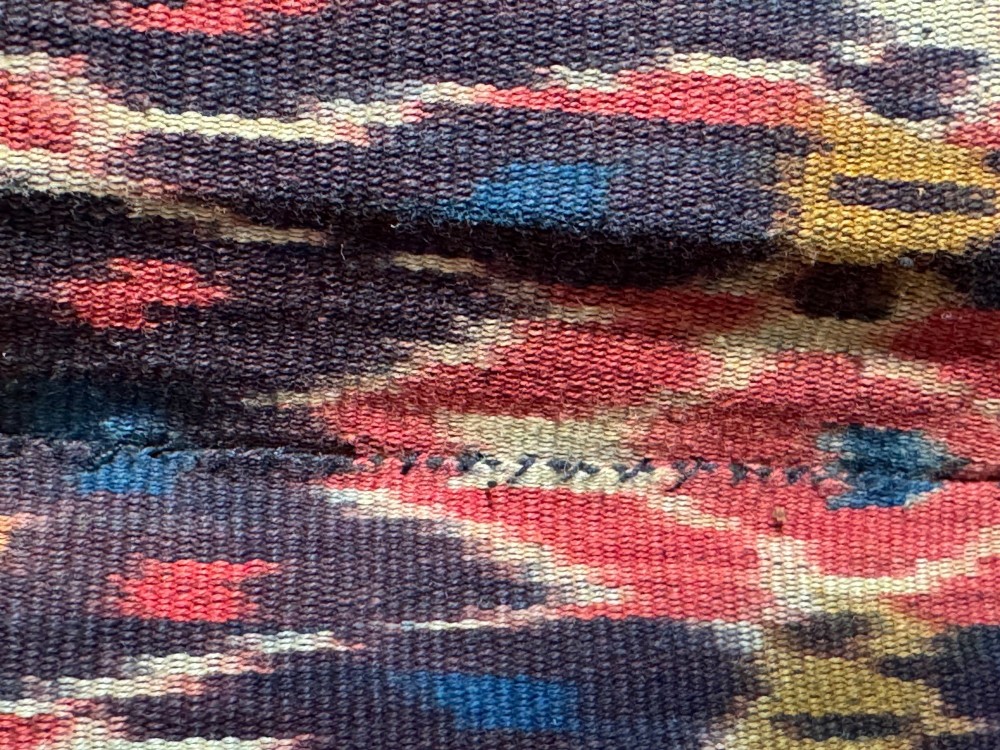 A vertical handwoven Sumba ikat hinggi textile featuring diamond lattice patterns in terracotta red, dark indigo, and yellow with zoomorphic border bands and lower fringe. View IV