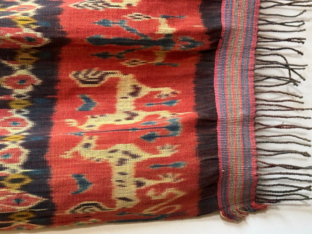 A vertical handwoven Sumba ikat hinggi textile featuring diamond lattice patterns in terracotta red, dark indigo, and yellow with zoomorphic border bands and lower fringe. View V