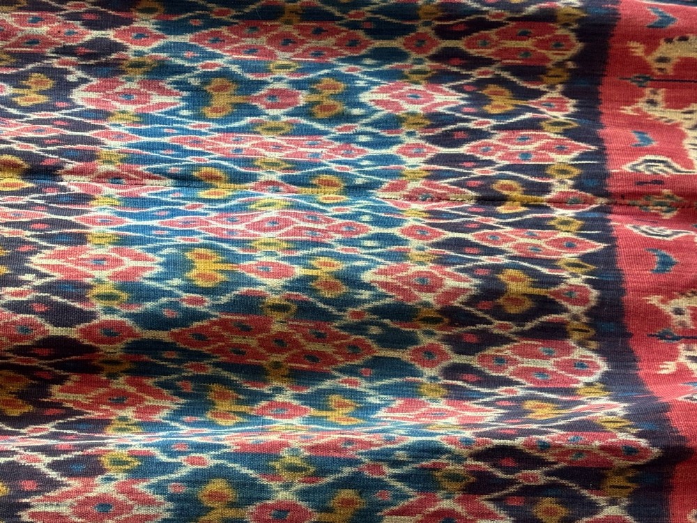 A vertical handwoven Sumba ikat hinggi textile featuring diamond lattice patterns in terracotta red, dark indigo, and yellow with zoomorphic border bands and lower fringe. View VI