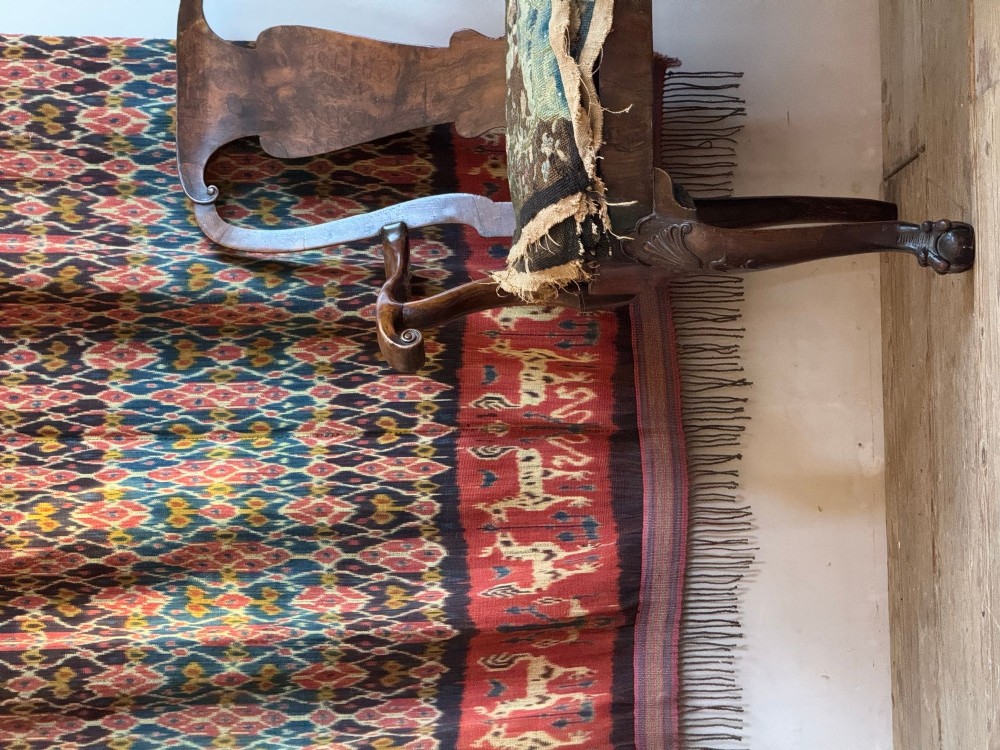 A vertical handwoven Sumba ikat hinggi textile featuring diamond lattice patterns in terracotta red, dark indigo, and yellow with zoomorphic border bands and lower fringe. View VII
