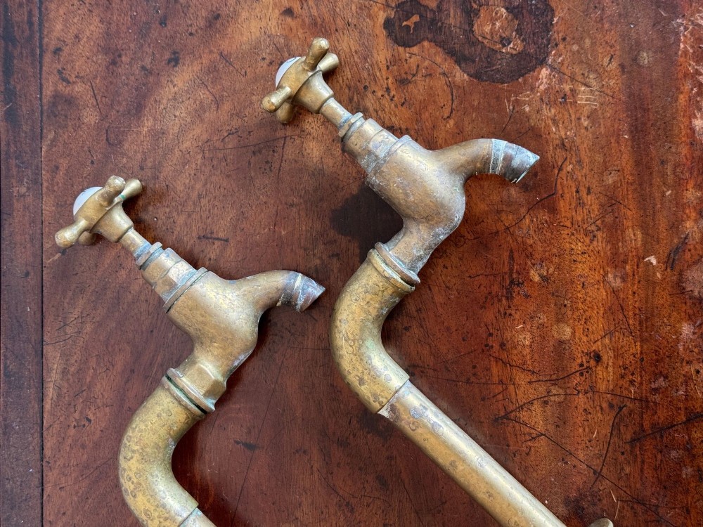 A pair of reclaimed antique brass bib taps with crosshead handles mounted on extended brass standpipes. View V