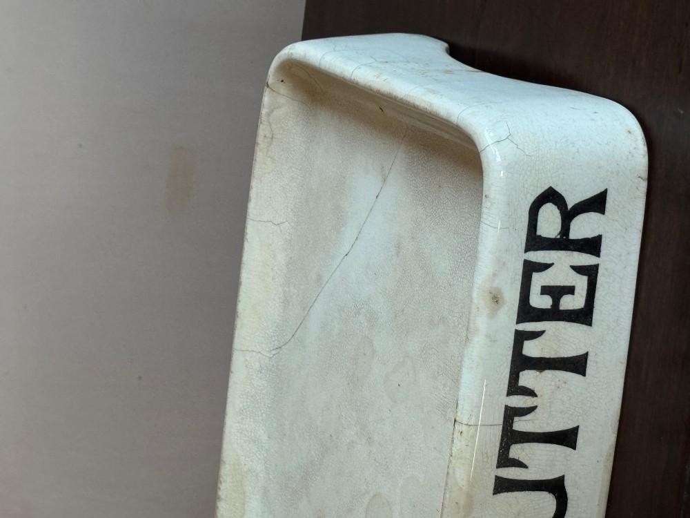 A rectangular cream ceramic grocers slab with black transfer-printed typography reading PURE BUTTER on the front edge. View VII