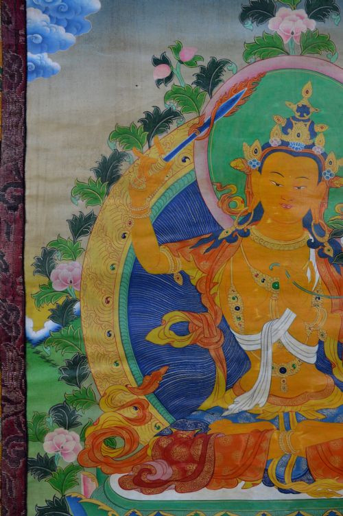 A Tibetan Thangka scroll depicting the seated deity Manjushri holding a raised sword and lotus stem, framed with a patterned silk border. View VI