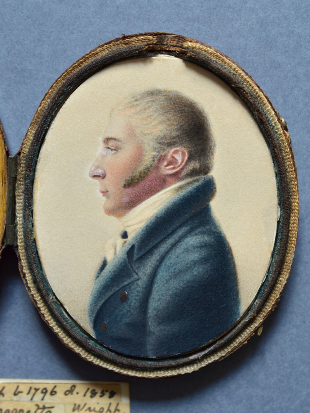An oval watercolour portrait miniature showing a profile view of a gentleman wearing a dark blue coat and white cravat set in a leather case.