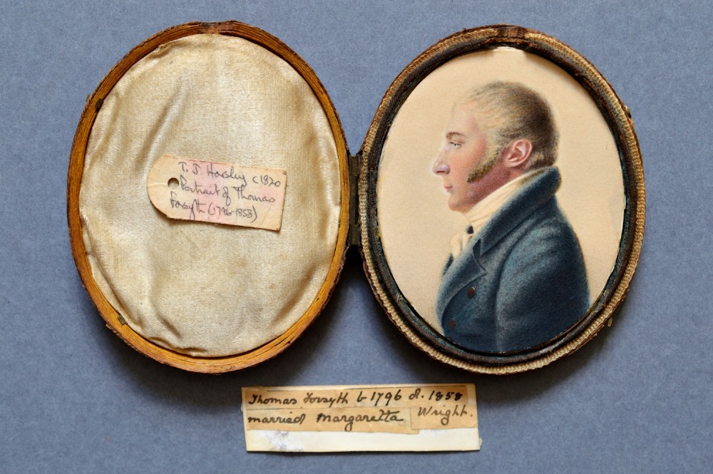 An oval watercolour portrait miniature showing a profile view of a gentleman wearing a dark blue coat and white cravat set in a leather case. View III