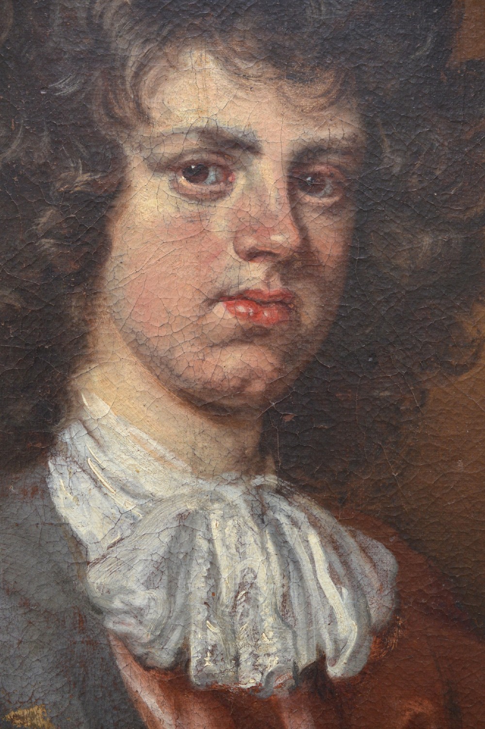 An antique oil portrait painting depicting a young gentleman with dark voluminous curls, wearing a white lace cravat and red mantle within a feigned oval frame. View V