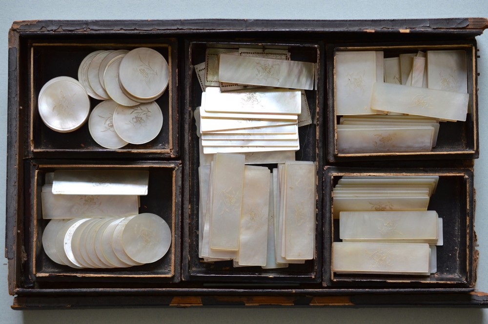 A collection of 126 engraved Chinese mother of pearl gaming counters in round and rectangular shapes arranged inside a fitted wooden tray.