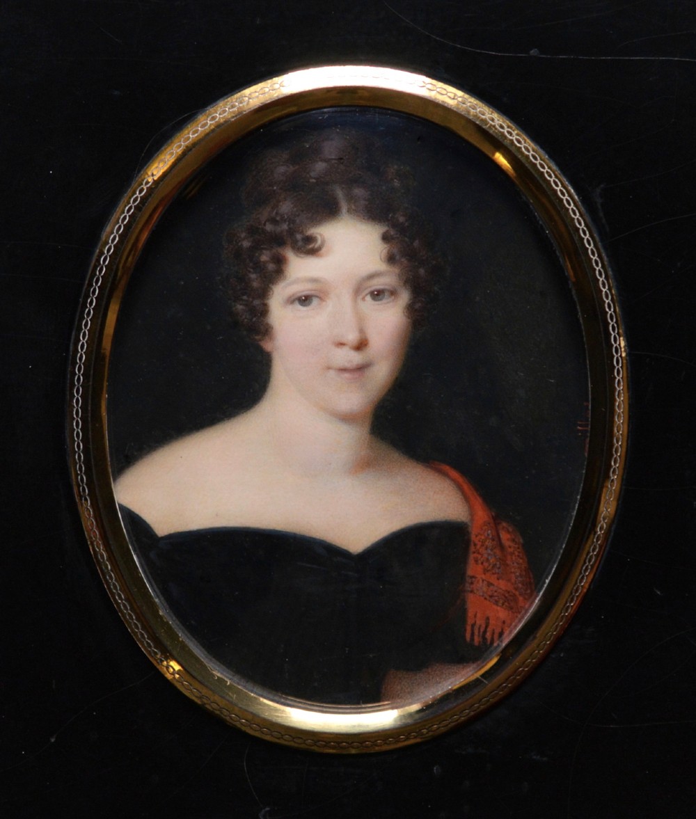 An oval portrait miniature painting depicting a woman with dark curly hair in a black off-the-shoulder dress, set in a beaded gilt brass bezel within a black frame.