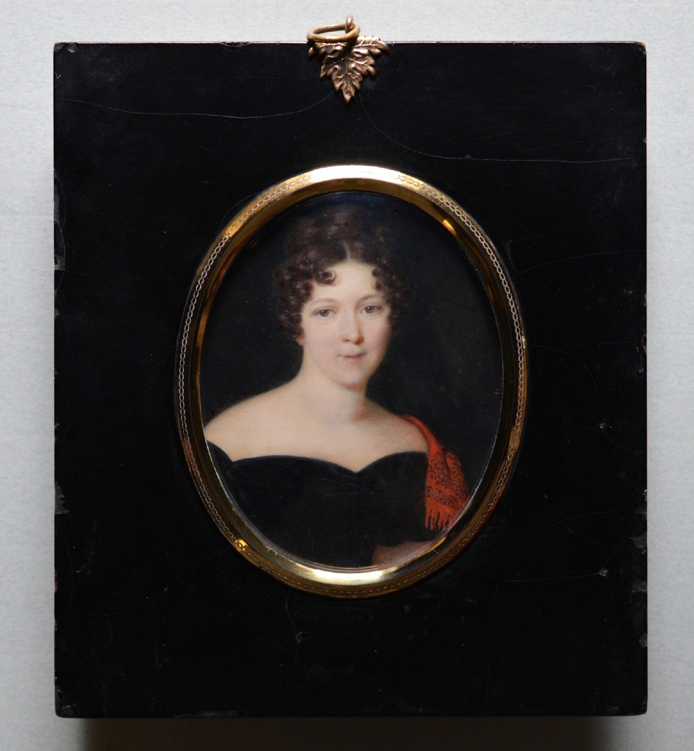 An oval portrait miniature painting depicting a woman with dark curly hair in a black off-the-shoulder dress, set in a beaded gilt brass bezel within a black frame. View II