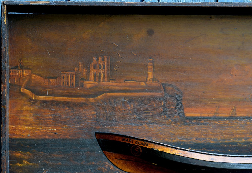 A 19th-century framed wooden folk art diorama featuring a relief-carved half hull coble boat set against a painted view of Tynemouth Castle and Priory. View II