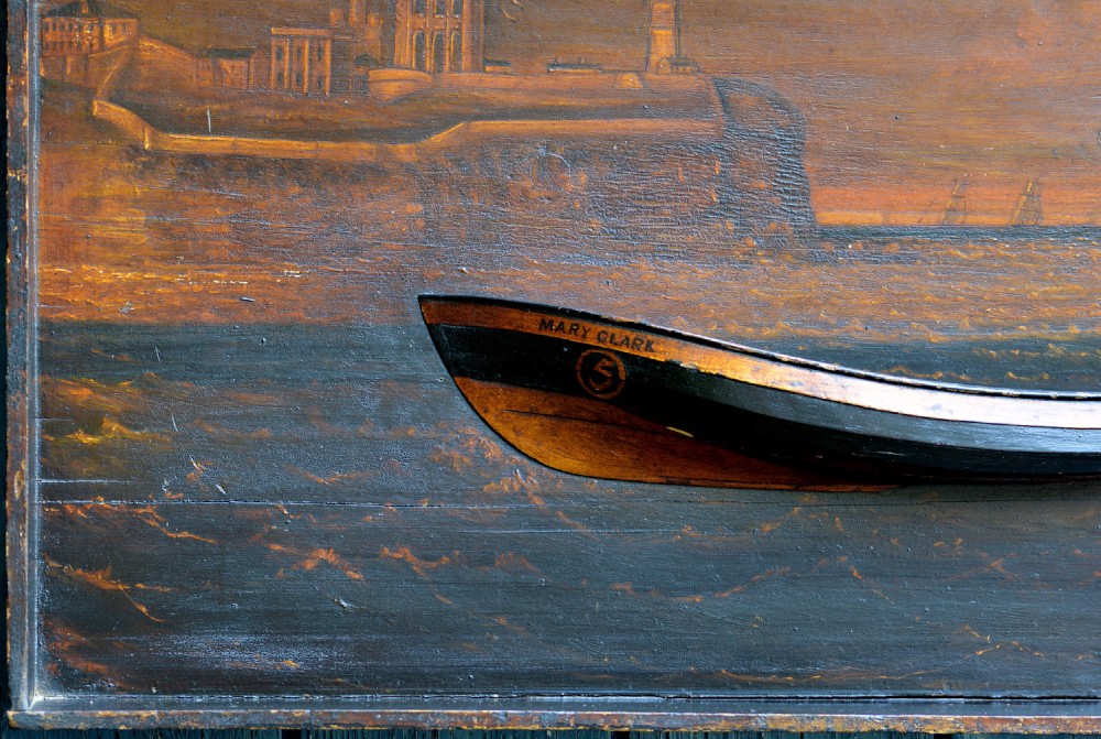 A 19th-century framed wooden folk art diorama featuring a relief-carved half hull coble boat set against a painted view of Tynemouth Castle and Priory. View III