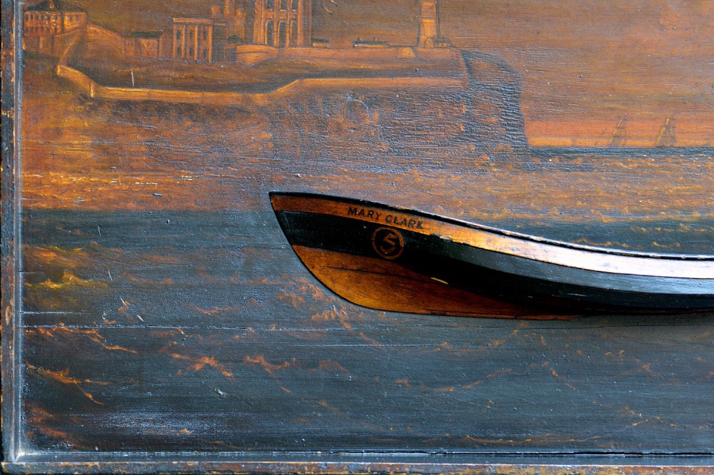 A 19th-century framed wooden folk art diorama featuring a relief-carved half hull coble boat set against a painted view of Tynemouth Castle and Priory. View VII