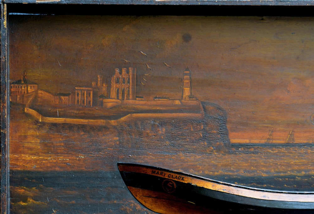 A 19th-century framed wooden folk art diorama featuring a relief-carved half hull coble boat set against a painted view of Tynemouth Castle and Priory. View VIII