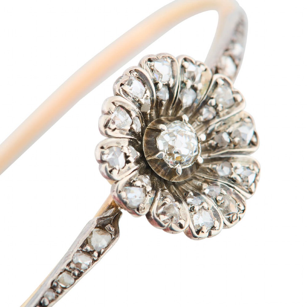 A hinged gold bangle featuring a central diamond-set floral cluster motif flanked by diamond-set shoulders.