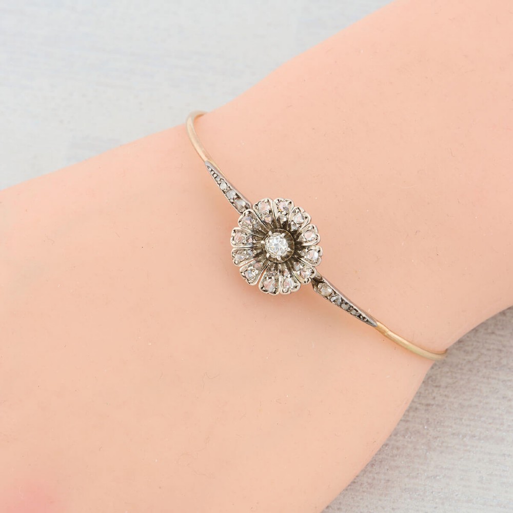 A hinged gold bangle featuring a central diamond-set floral cluster motif flanked by diamond-set shoulders. View II