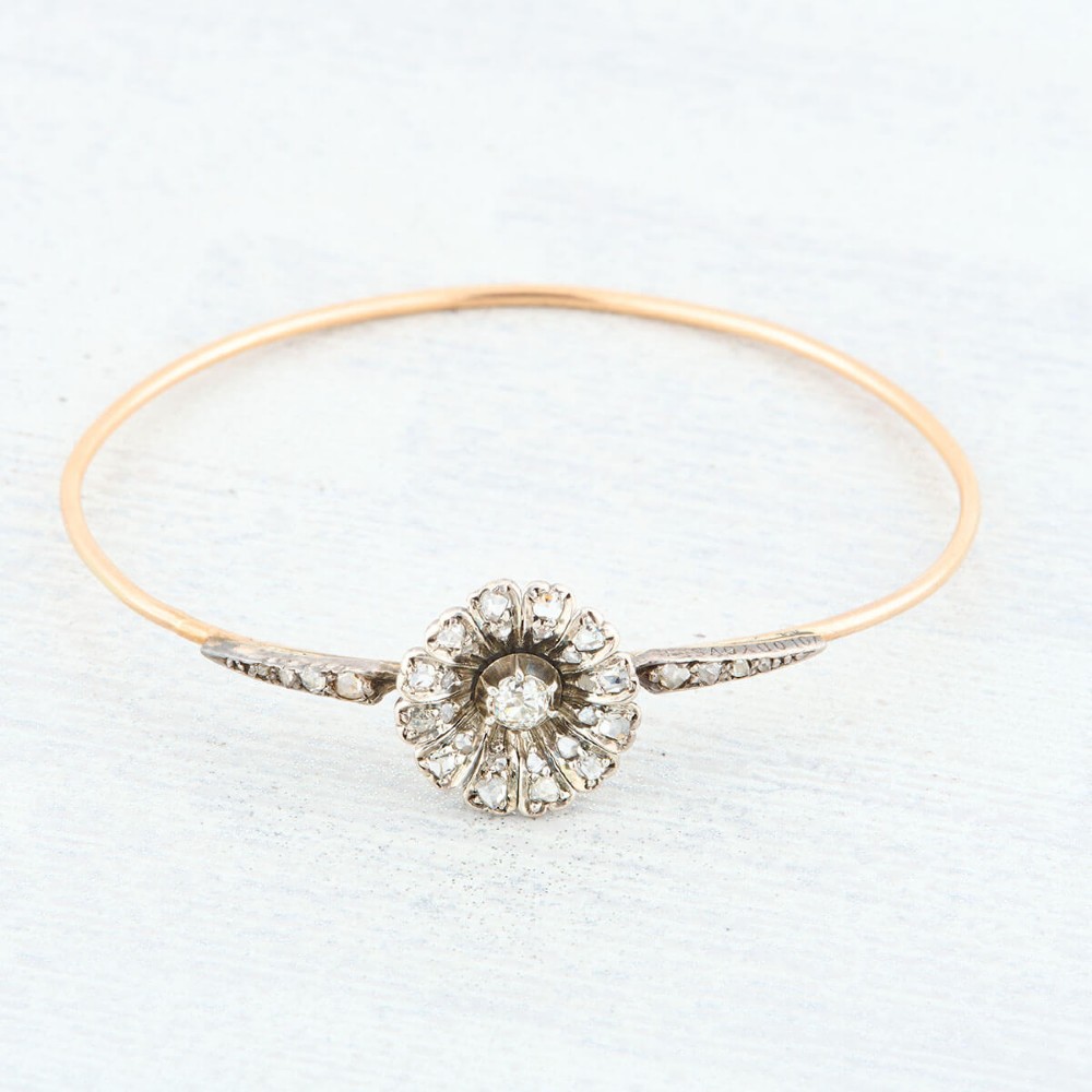 A hinged gold bangle featuring a central diamond-set floral cluster motif flanked by diamond-set shoulders. View III
