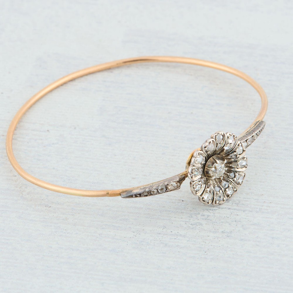 A hinged gold bangle featuring a central diamond-set floral cluster motif flanked by diamond-set shoulders. View IV