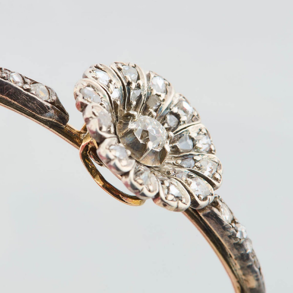 A hinged gold bangle featuring a central diamond-set floral cluster motif flanked by diamond-set shoulders. View V