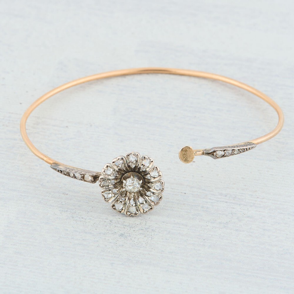 A hinged gold bangle featuring a central diamond-set floral cluster motif flanked by diamond-set shoulders. View VII