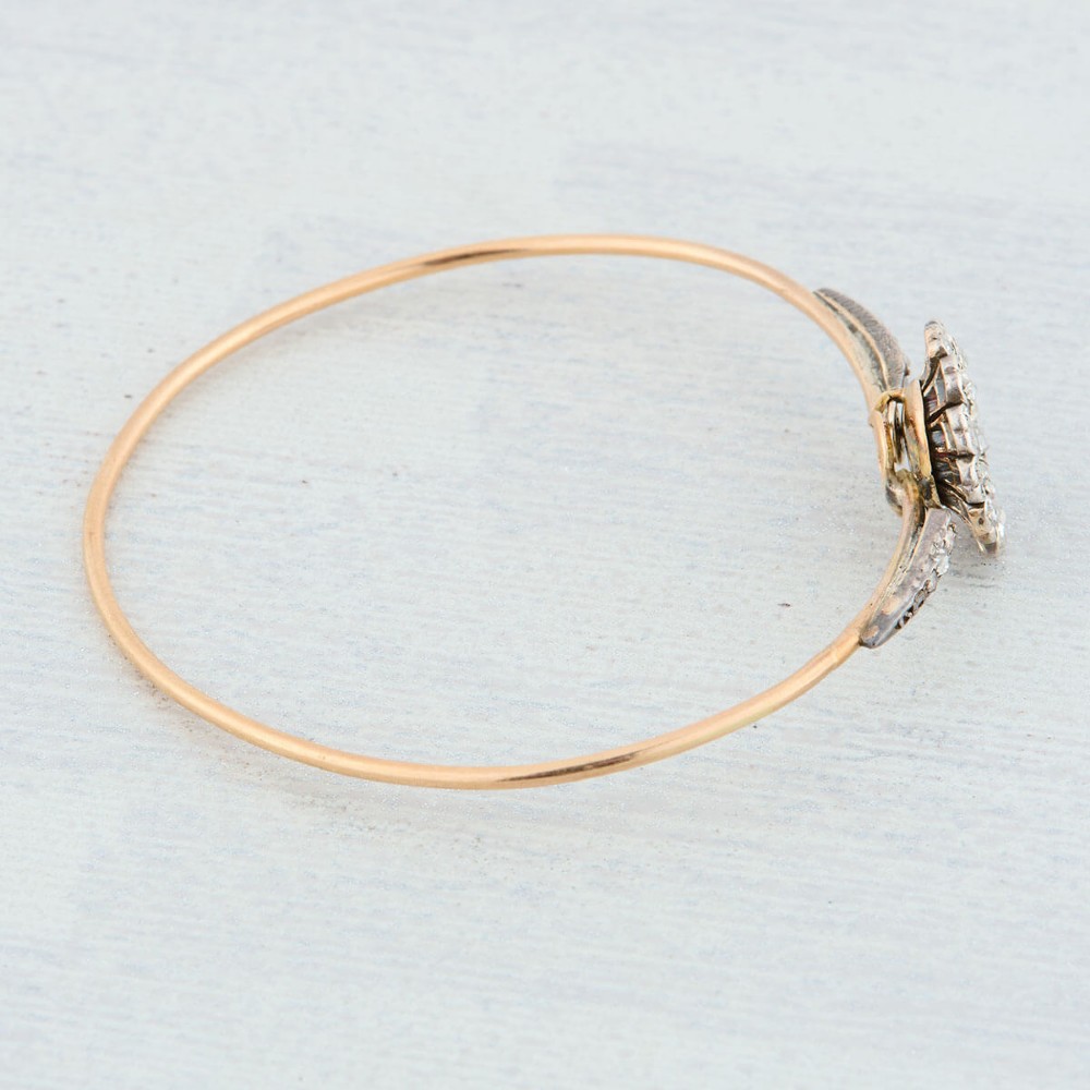 A hinged gold bangle featuring a central diamond-set floral cluster motif flanked by diamond-set shoulders. View VIII