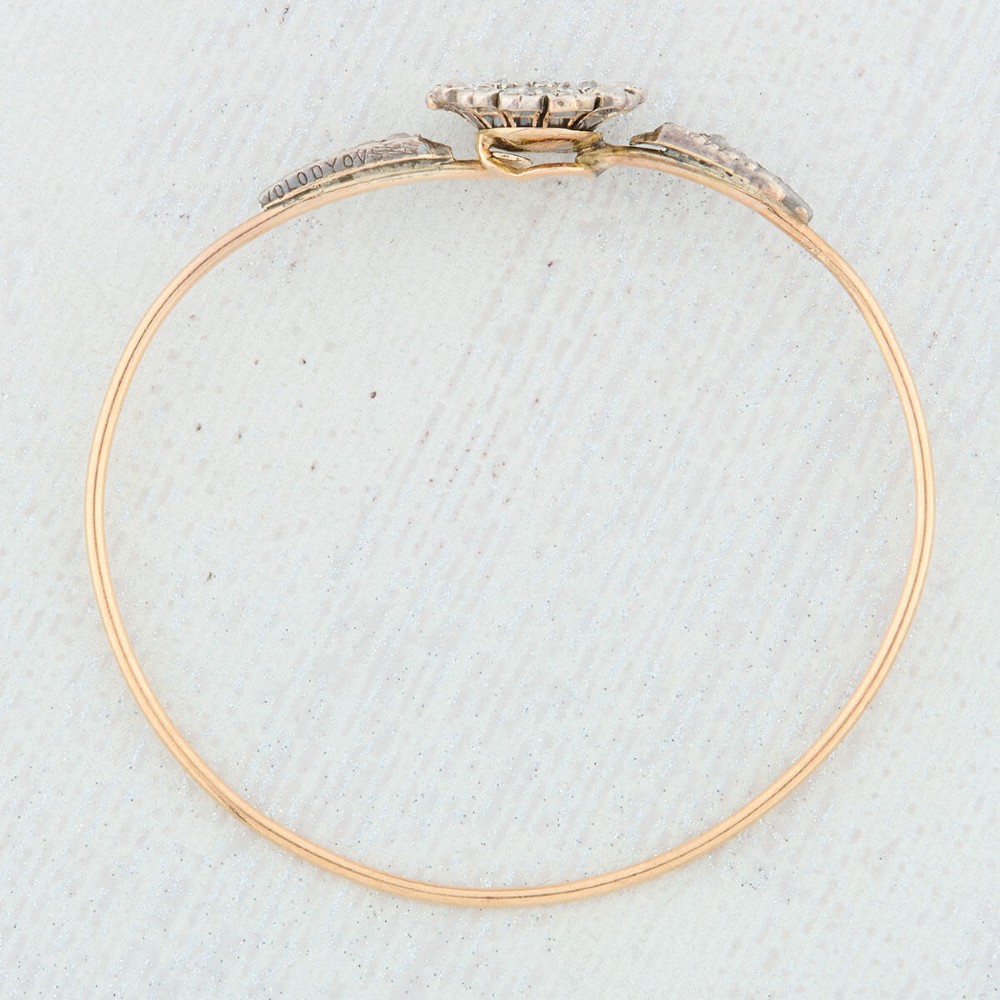 A hinged gold bangle featuring a central diamond-set floral cluster motif flanked by diamond-set shoulders. View IX