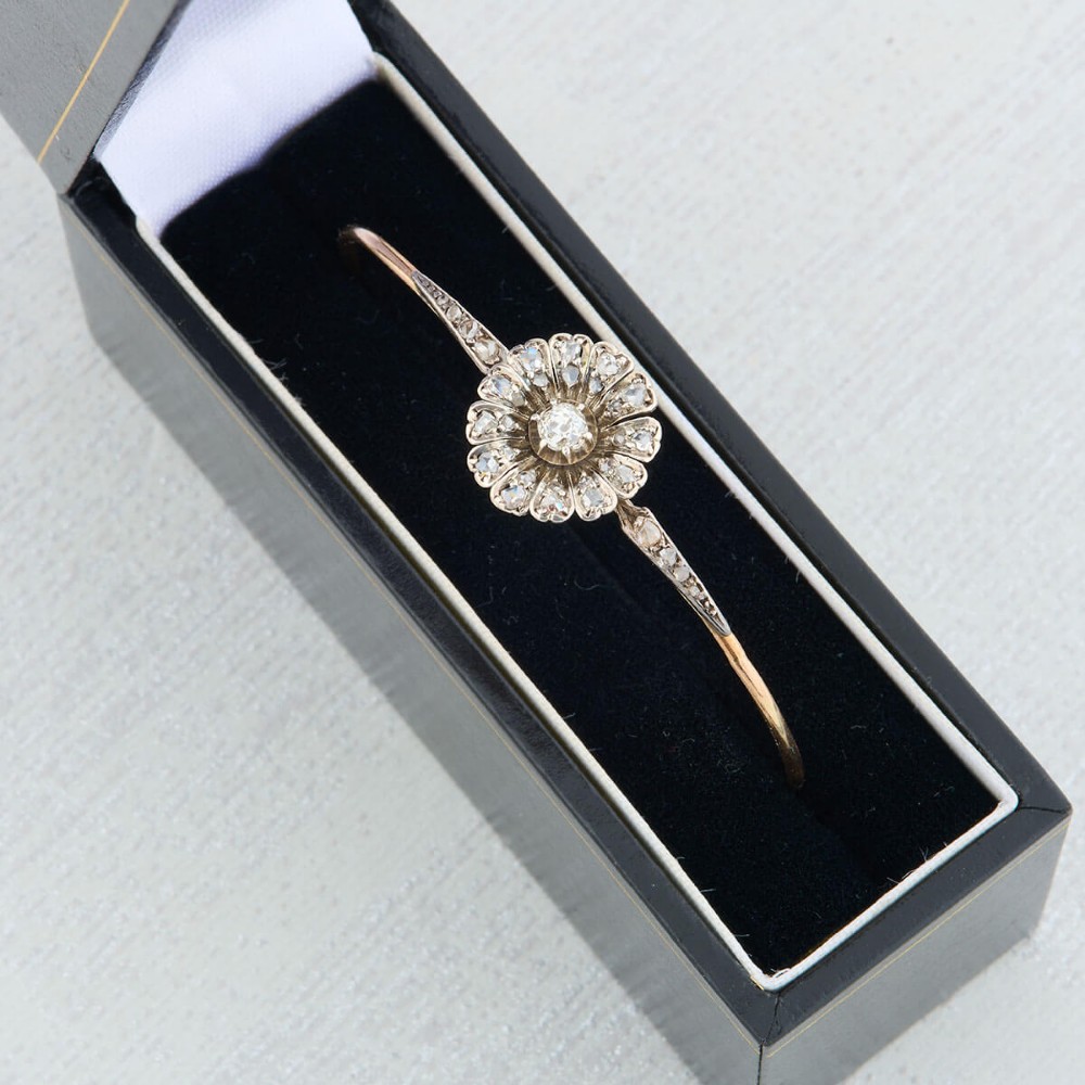 A hinged gold bangle featuring a central diamond-set floral cluster motif flanked by diamond-set shoulders. View X