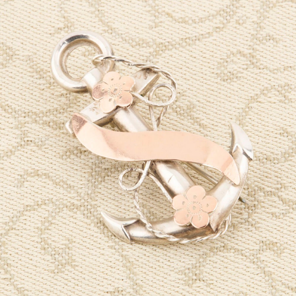 An antique silver anchor brooch featuring coiled rope wirework, two rose gold flowers, and a blank central rose gold scroll banner.