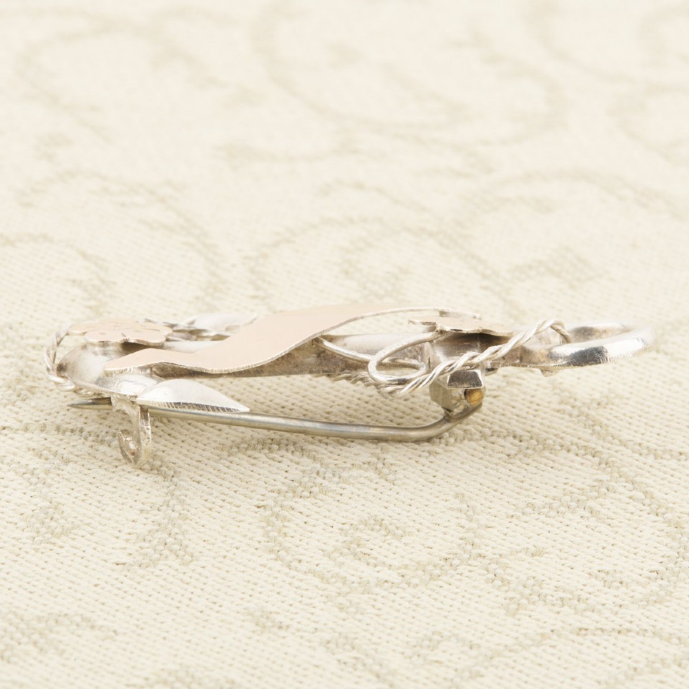 An antique silver anchor brooch featuring coiled rope wirework, two rose gold flowers, and a blank central rose gold scroll banner. View V