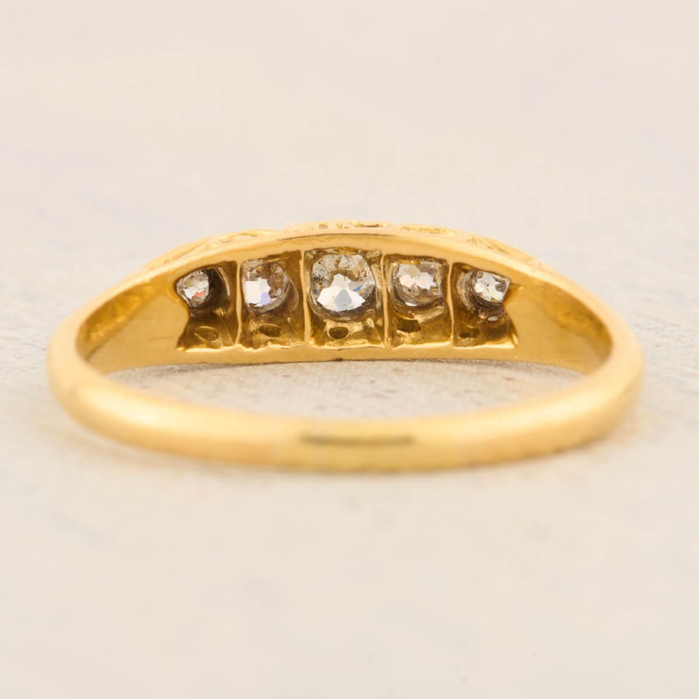 An antique 18ct yellow gold ring featuring five graduated round cut diamonds set in a carved gold gallery. View VI