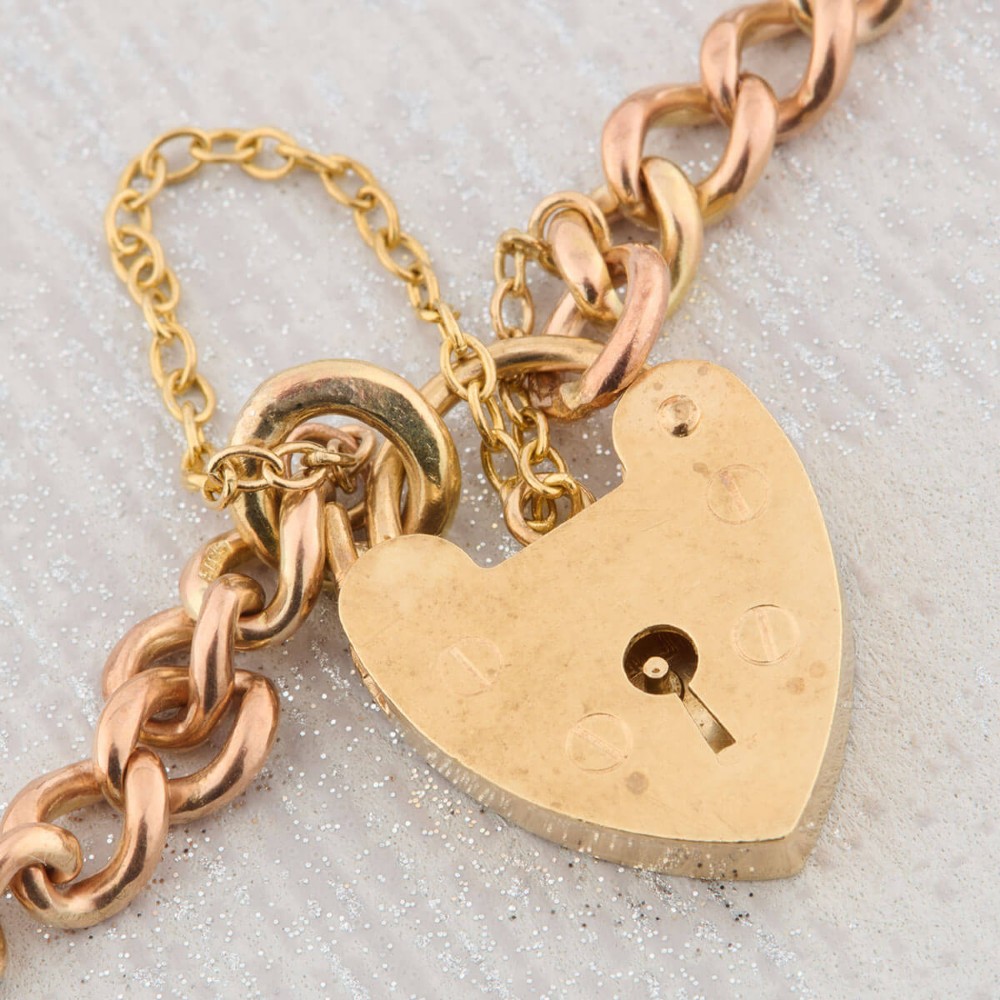 A 9ct rose gold curb chain bracelet featuring a heart-shaped padlock clasp with an attached safety chain. View III