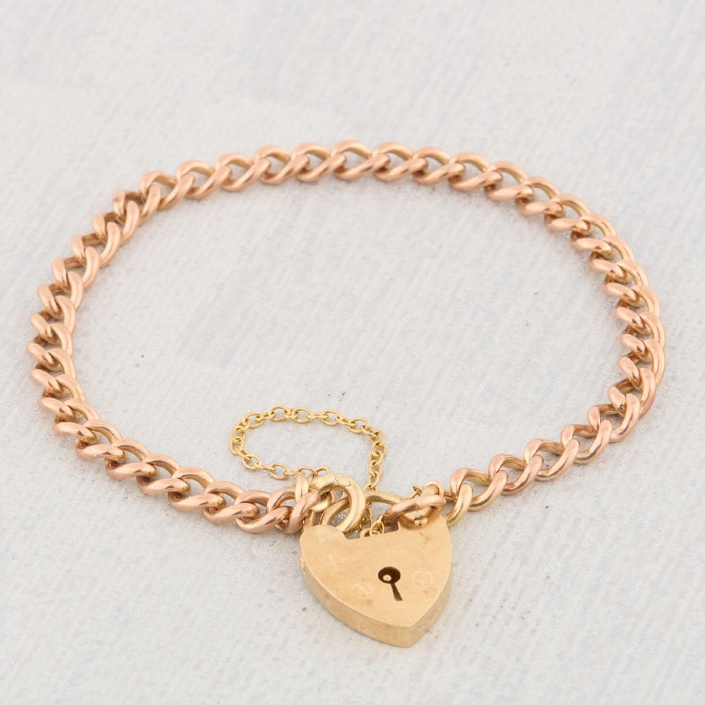 A 9ct rose gold curb chain bracelet featuring a heart-shaped padlock clasp with an attached safety chain. View IV