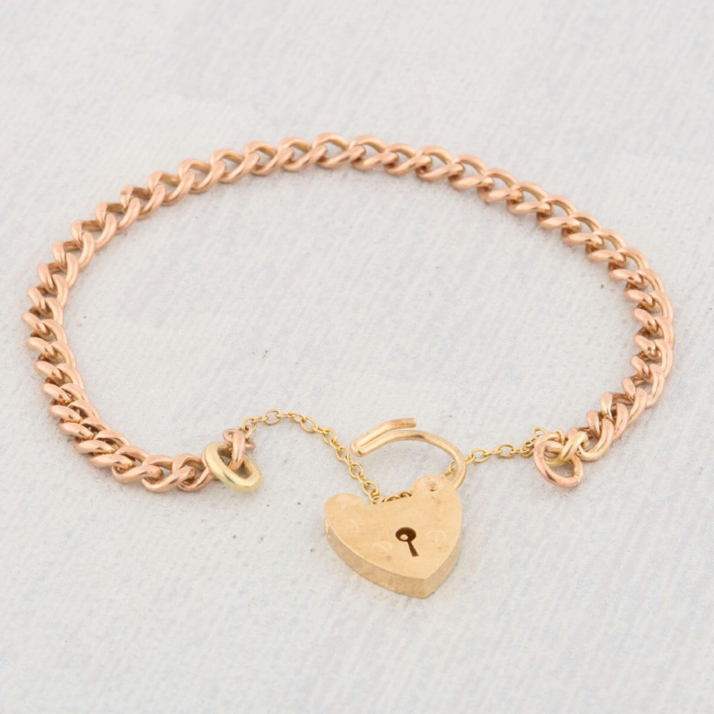 A 9ct rose gold curb chain bracelet featuring a heart-shaped padlock clasp with an attached safety chain. View V