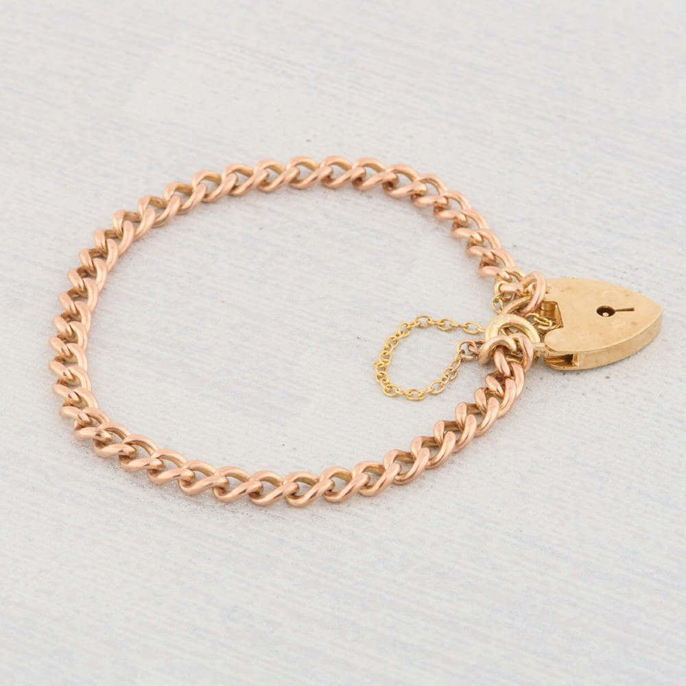 A 9ct rose gold curb chain bracelet featuring a heart-shaped padlock clasp with an attached safety chain. View VI